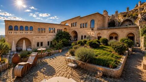 A courtyard with stone flooring, outdoor seating, and a building with arches and windows. - Hush Cappadocia (Urgup)