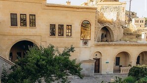 Ein Innenhof mit einer großen Felsformation, einem Gebäude mit Rundbogenfenstern und einer Steintreppe.