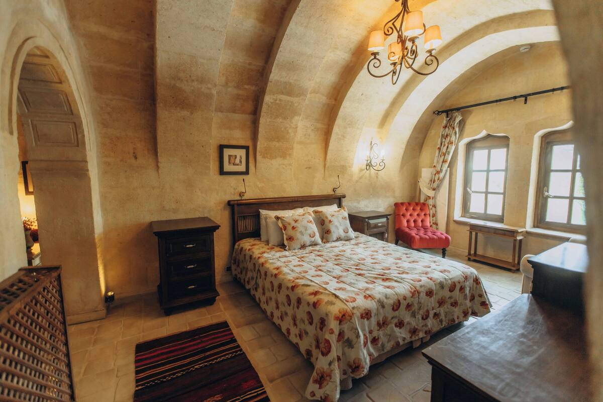 A bedroom with a bed, a chair, a desk, and a fireplace.