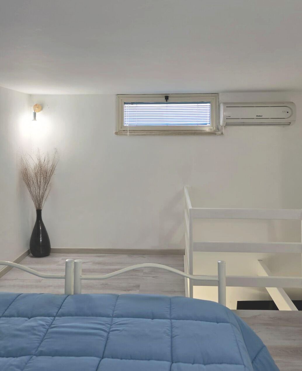 Una camera da letto con un letto, una finestra, un condizionatore e un vaso con dei rami.