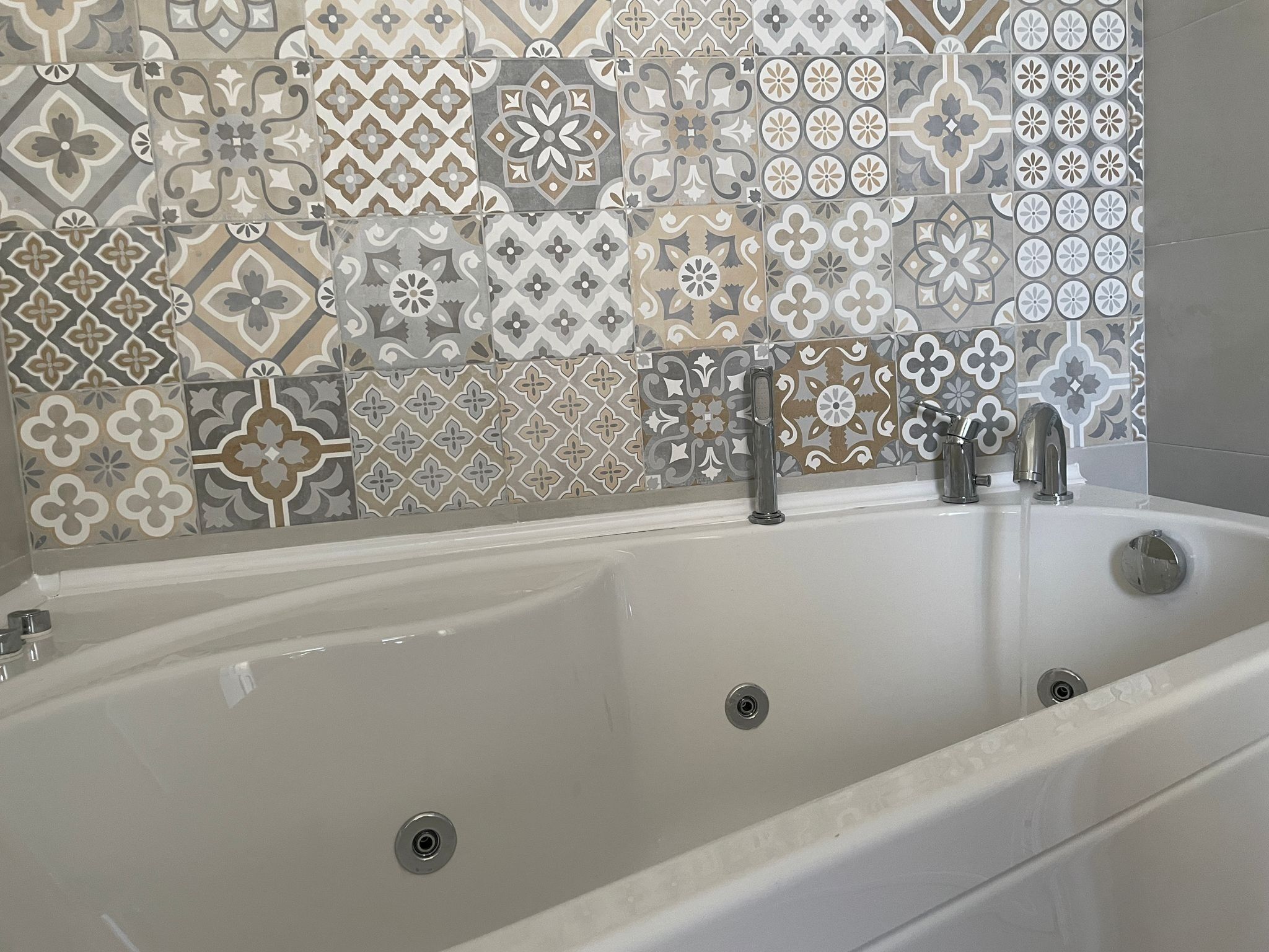 A bathroom with a bathtub, two faucets, and a tiled wall with various patterns.