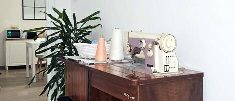 A wooden desk with a sewing machine, a plant, and framed pictures on the wall.