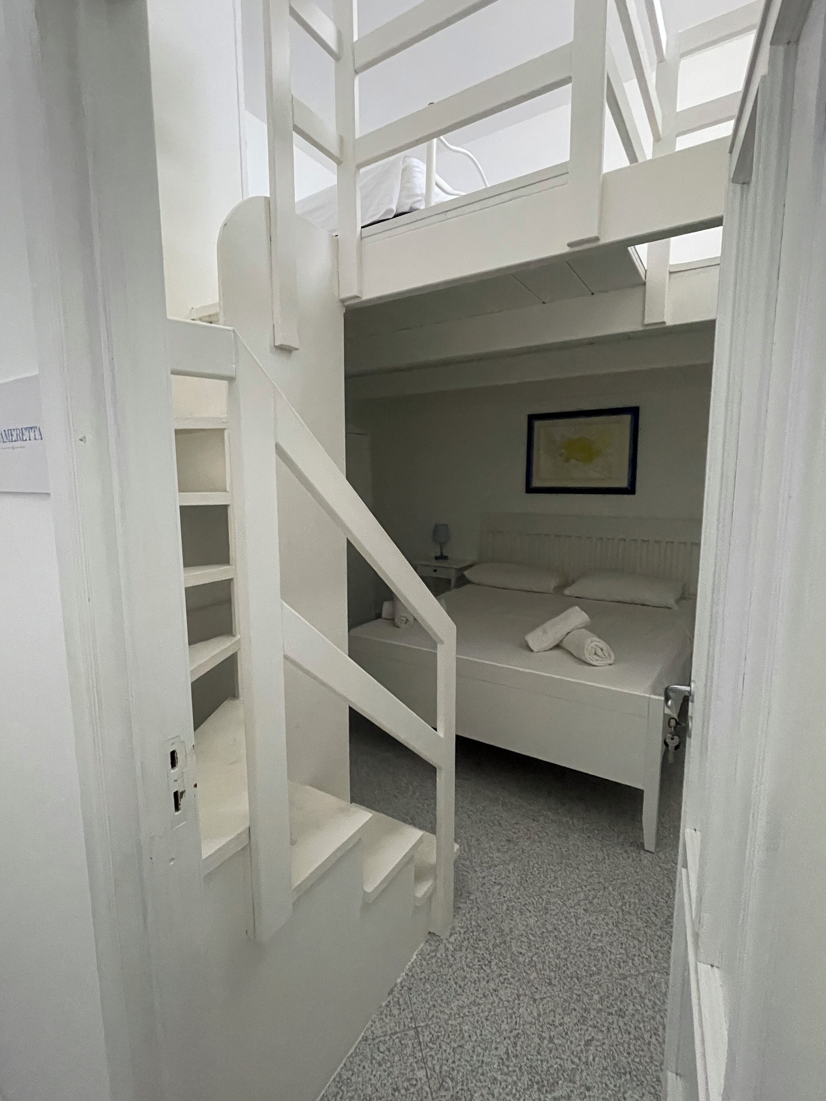 Habitación con literas y una escalera blanca que lleva a una entreplanta.
