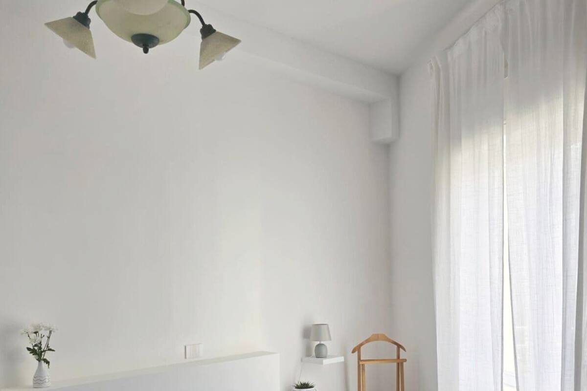 Un dormitorio con una colcha azul, una mesita de noche con una lámpara, una planta pequeña y una silla de madera.