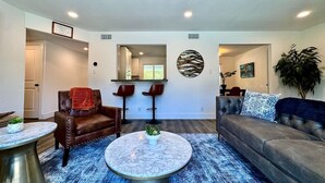 A living room with a sofa, two chairs, a coffee table, and a dining area with a bench. - 4BR · Pool · Fenced Yard · Garage · Tree-Lined Street (Carmichael)