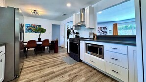 A modern kitchen with white cabinets, a stainless steel refrigerator, and a dining area with a wooden table and chairs. - 4BR · Pool · Fenced Yard · Garage · Tree-Lined Street (Carmichael)