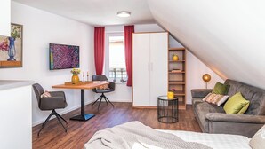 A modern loft bedroom with a sloped ceiling, a wooden dining table, a gray sofa, and a white wardrobe. - Zum Brandenburger Tor 18 (Damme)