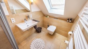 A modern bathroom with a skylight, a sink, a toilet, and a shower area. - Zum Brandenburger Tor 18 (Damme)