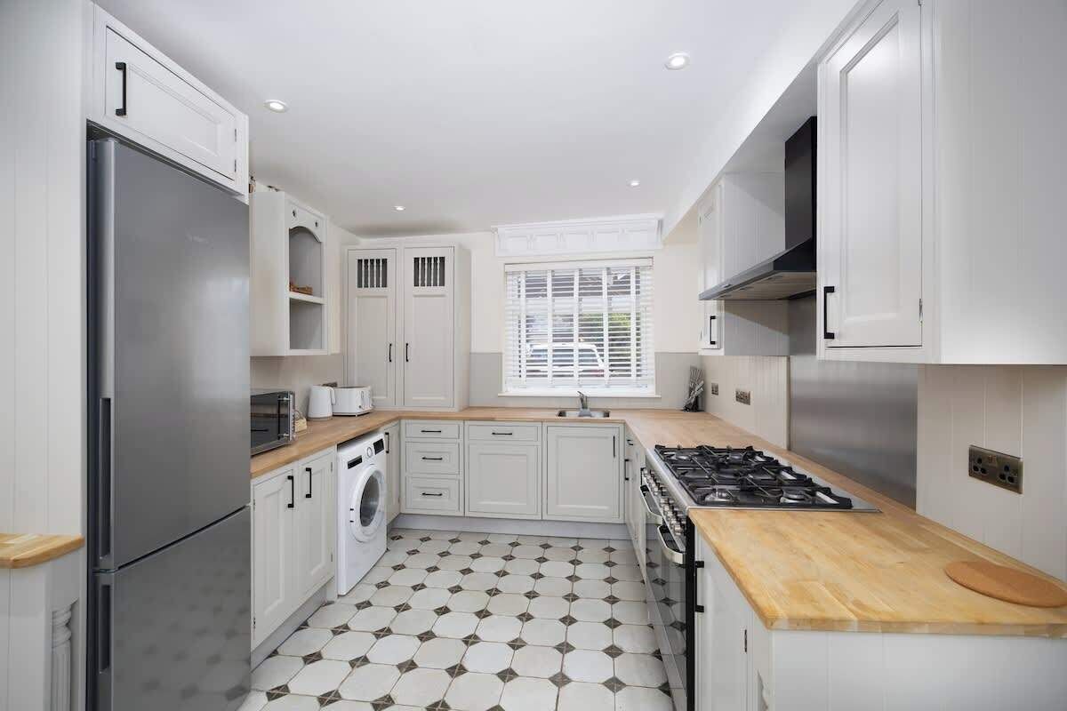 A modern kitchen with white cabinetry, a stainless steel refrigerator, a built-in oven, and a wooden countertop.