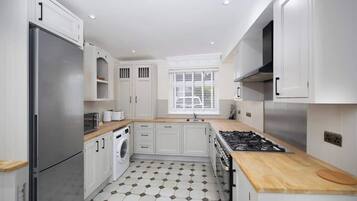 A modern kitchen with white cabinetry, a stainless steel refrigerator, a built-in oven, and a wooden countertop.