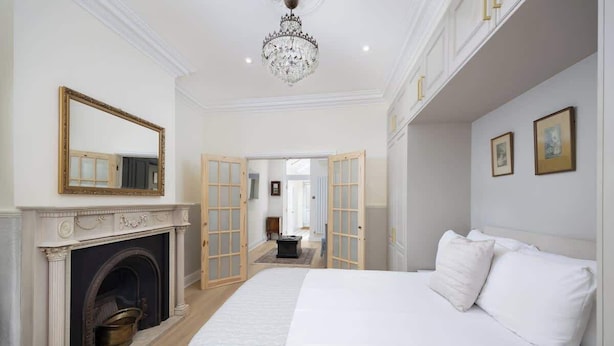 A bedroom with a fireplace, a large bed, a chandelier, and a hallway leading to another room. - Stunning Apartment | Lincoln City Centre | Parking (Lincoln)