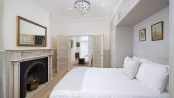 A bedroom with a fireplace, a large bed, a chandelier, and a hallway leading to another room.