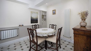 A dining area with a round table, six chairs, a radiator, a white tiled floor, a wooden cabinet, and a vase with dried flowers. - Stunning Apartment | Lincoln City Centre | Parking (Lincoln)