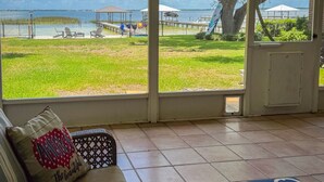 A room with a large window overlooking a grassy area and a body of water. There is a sofa with a cushion that has 'America the Beautiful' written on it.