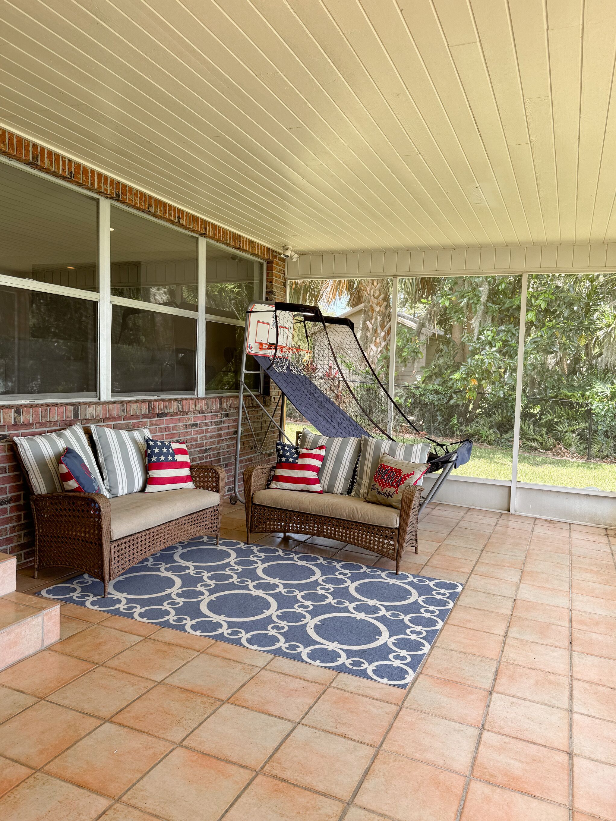A covered patio with two wicker sofas, a basketball hoop, and a patterned rug.