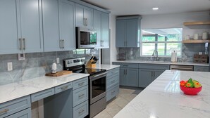 A modern kitchen with light blue cabinets, a white marble countertop, and stainless steel appliances.