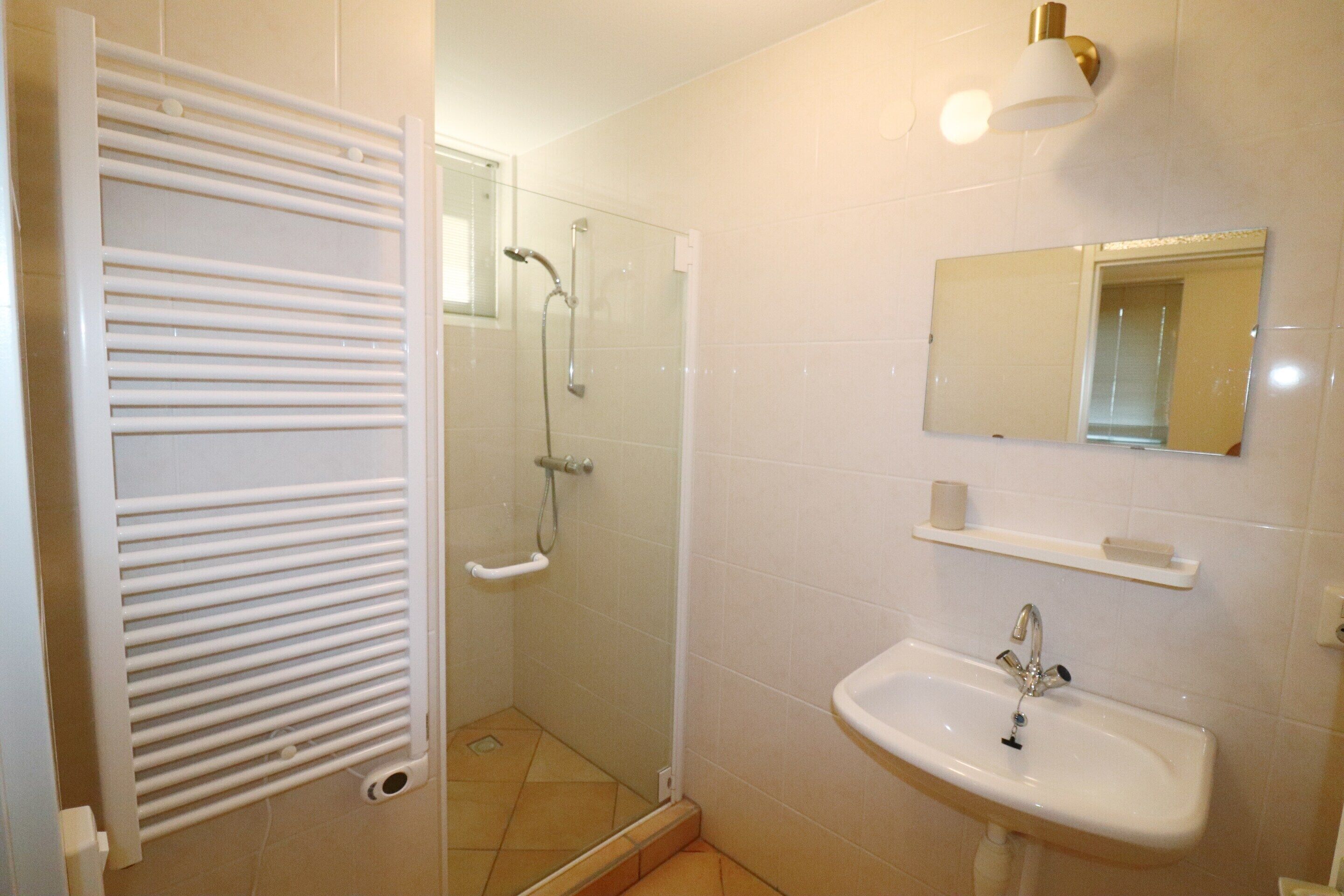 A bathroom with a shower, a sink, a mirror, and a towel rack.