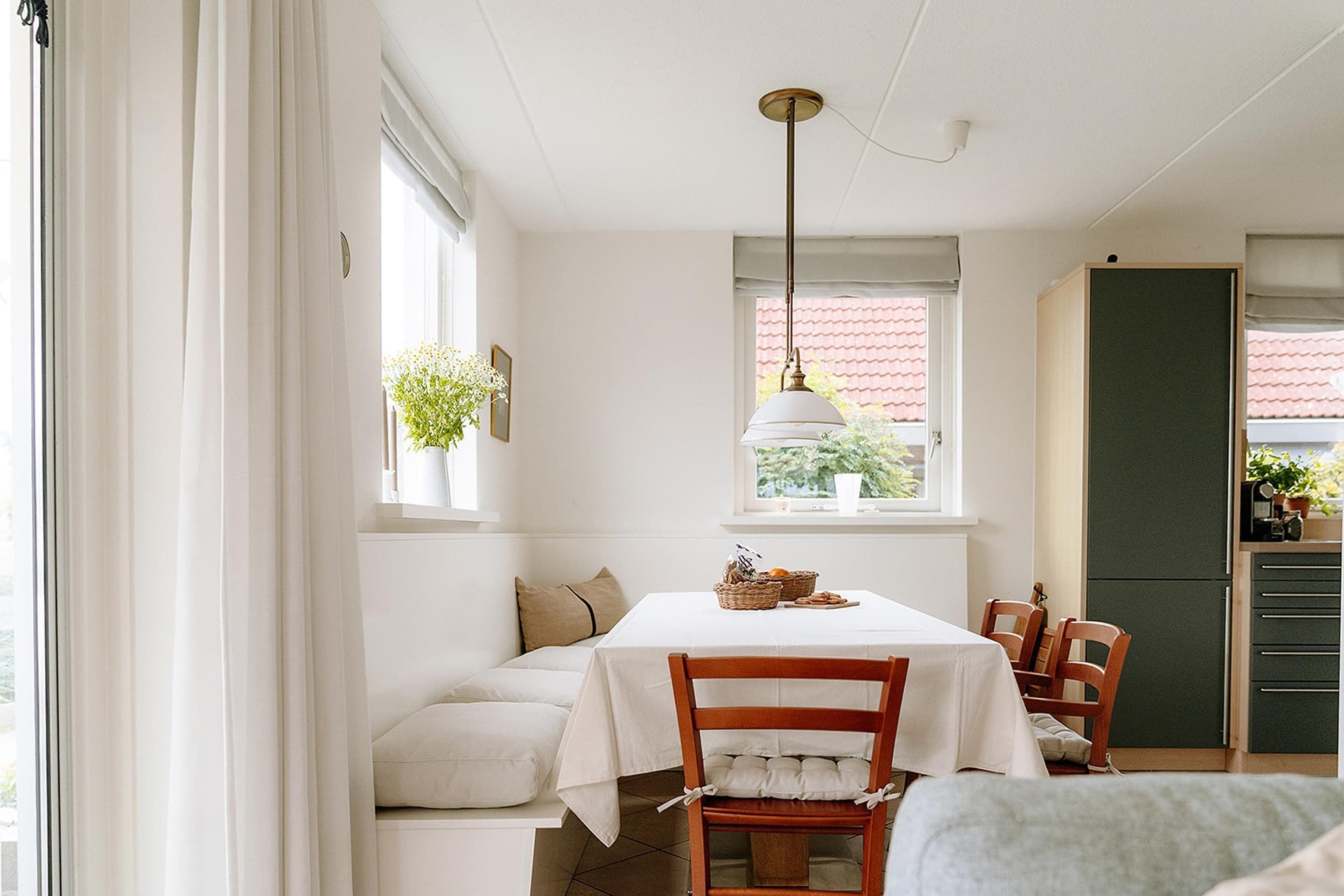Un coin repas avec une table dressée pour quatre personnes, un banc et un espace cuisine équipé de placards et d’un réfrigérateur.