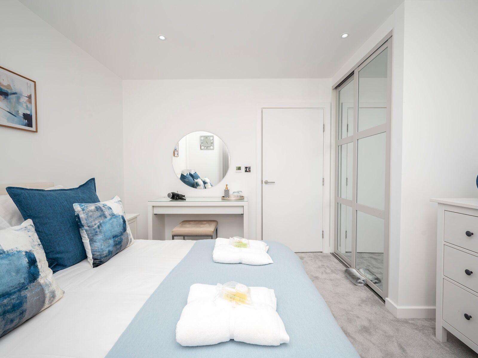 Quarto moderno com cama, mesa de cabeceira, espelho, guarda-roupa e banheiro.