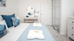 Een moderne slaapkamer met een bed, nachtkastje, spiegel, kledingkast en een badkamer.