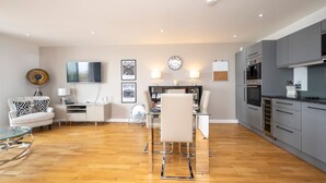 Een moderne woonkamer met een eethoek, een keuken en een aan de muur bevestigde televisie.