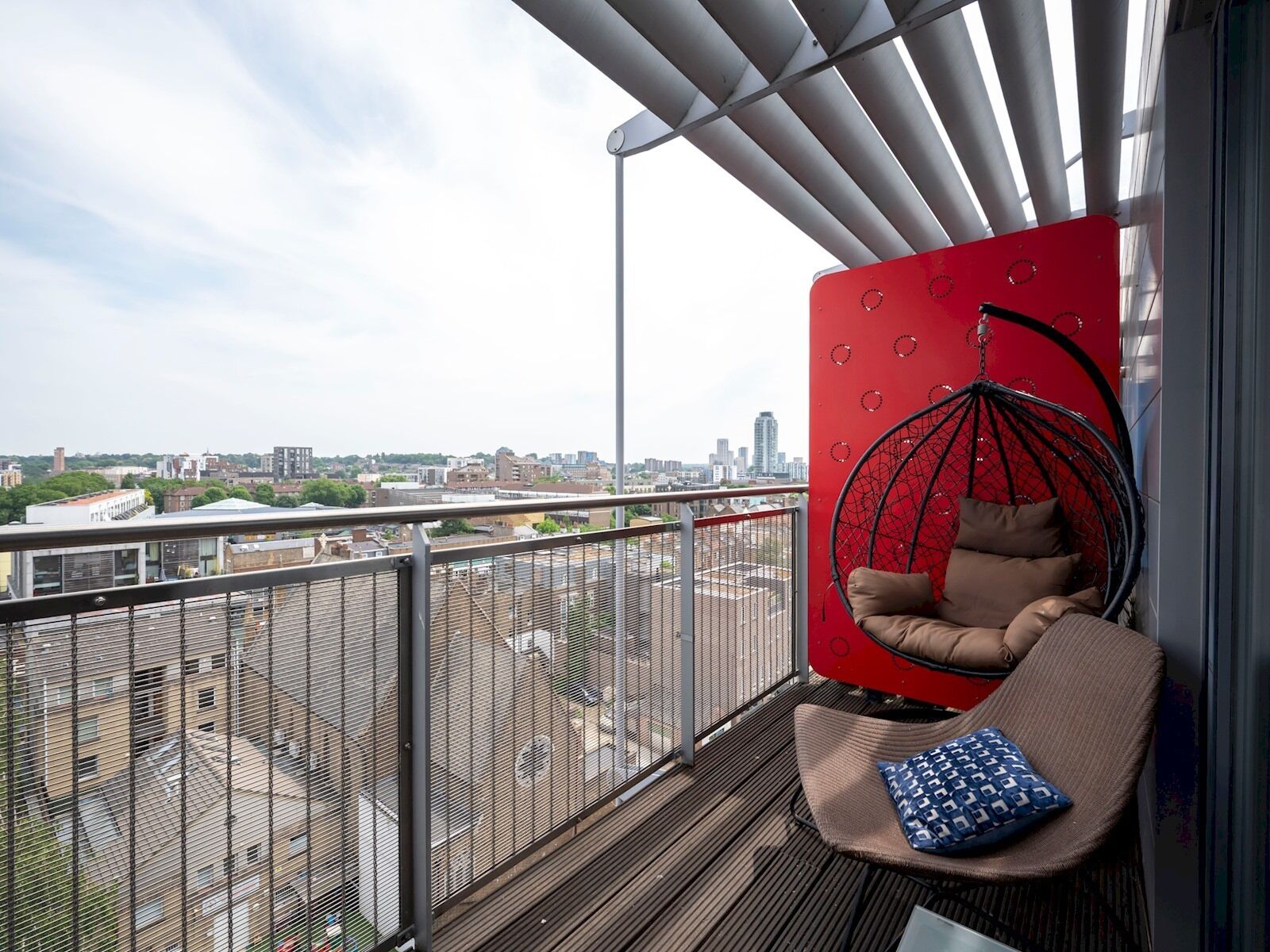 A balcony with a hanging chair, a red wall, and a city view.