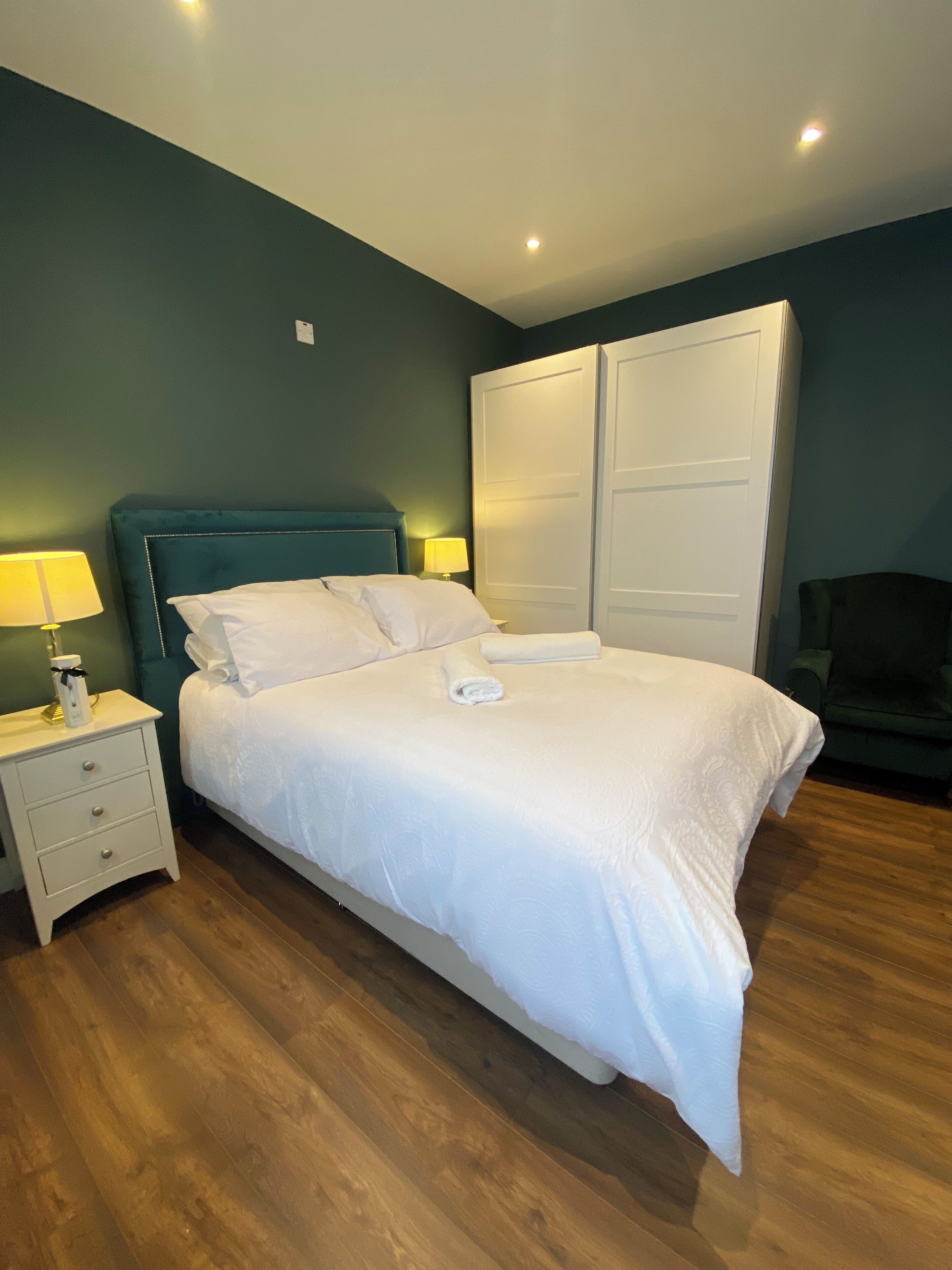A neatly made bed with white linens, a bedside table with a lamp, and a wardrobe with sliding doors.