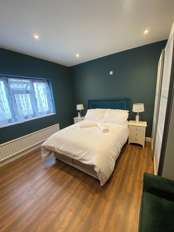 A bedroom with a bed, nightstands, a window with curtains, and a green wall.