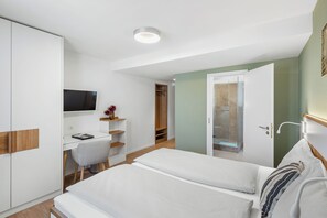 Et hotelværelse med seng, skrivebord, stol, fjernsyn og et klædeskab.