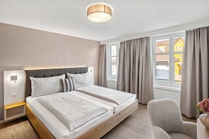 Et moderne hotelværelse med en stor seng, et sengebord, en stol og et vindue med gardiner.