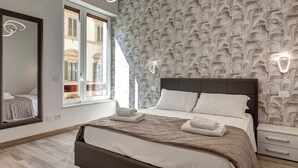 Una habitación de hotel moderna con una cama grande, una mesita de noche, un espejo y un papel tapiz estampado.