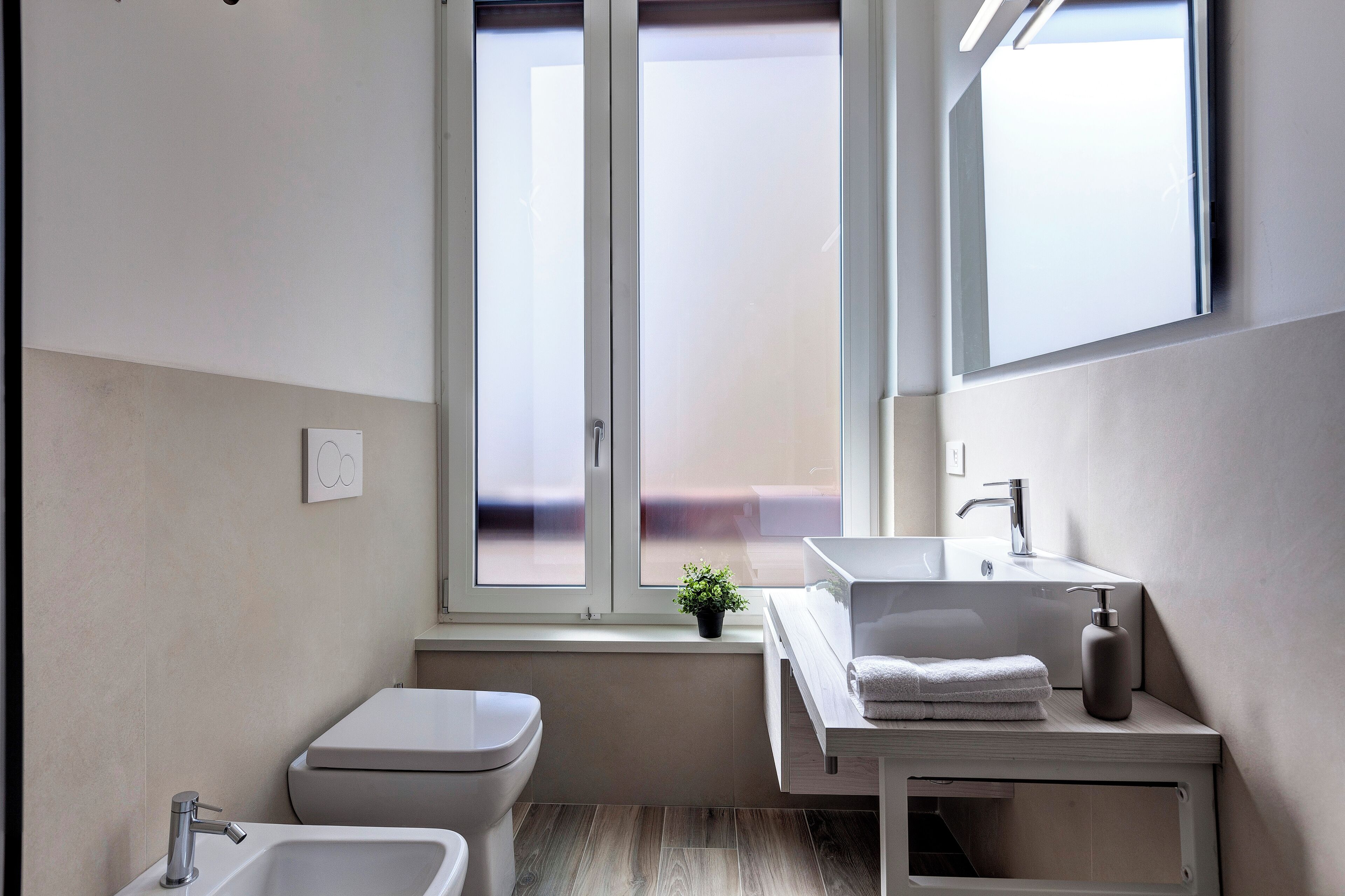 A modern bathroom with a toilet, bidet, sink, and window.