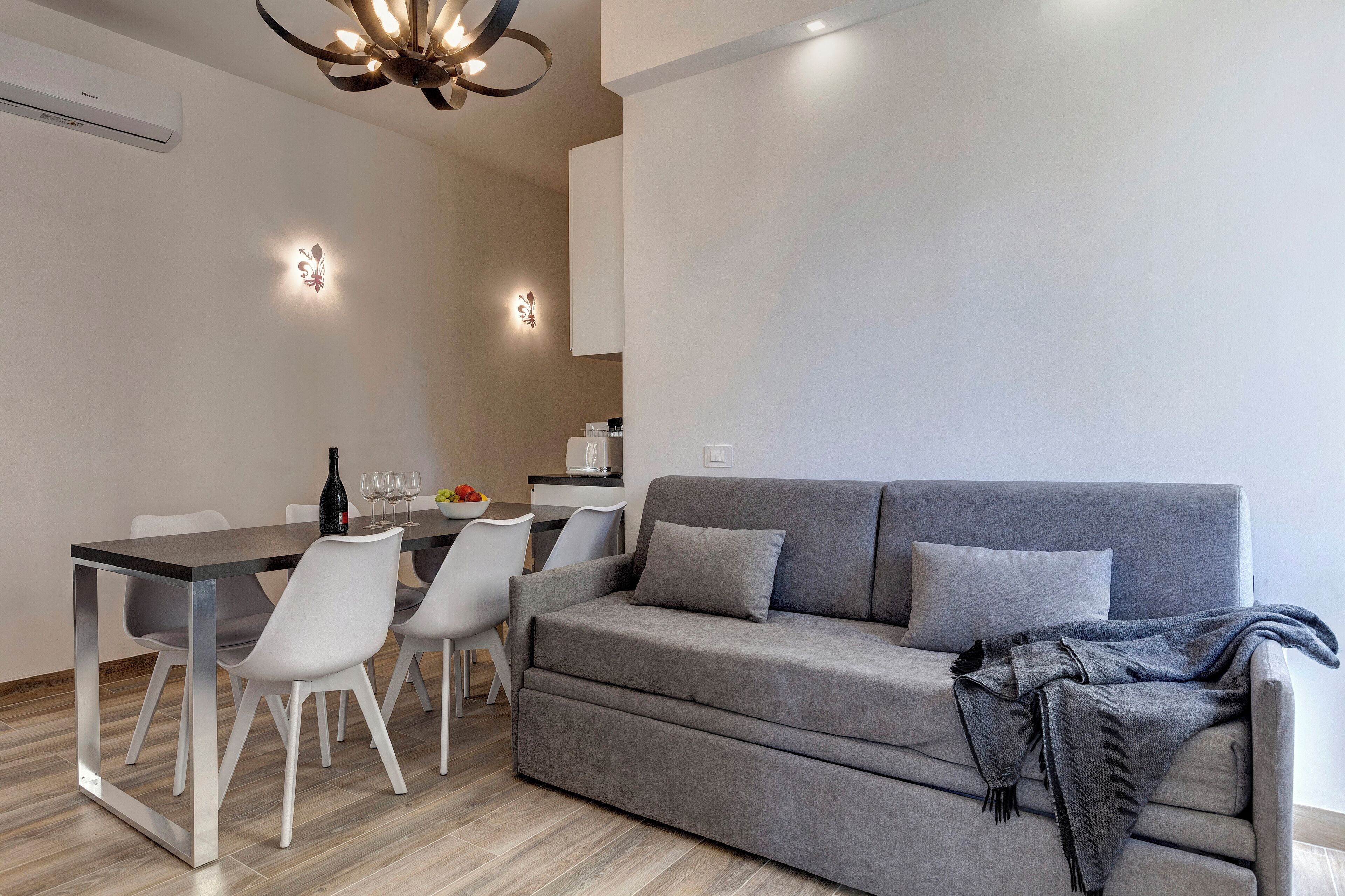 A modern living room with a grey sofa, white chairs, a dining table, and a chandelier.