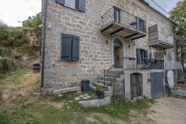 A stone building with a balcony, a door, and a small garden area.