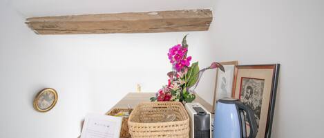 Une table en bois, un panier en osier, une photographie encadrée, une bouilloire bleue et un petit vase avec des fleurs.