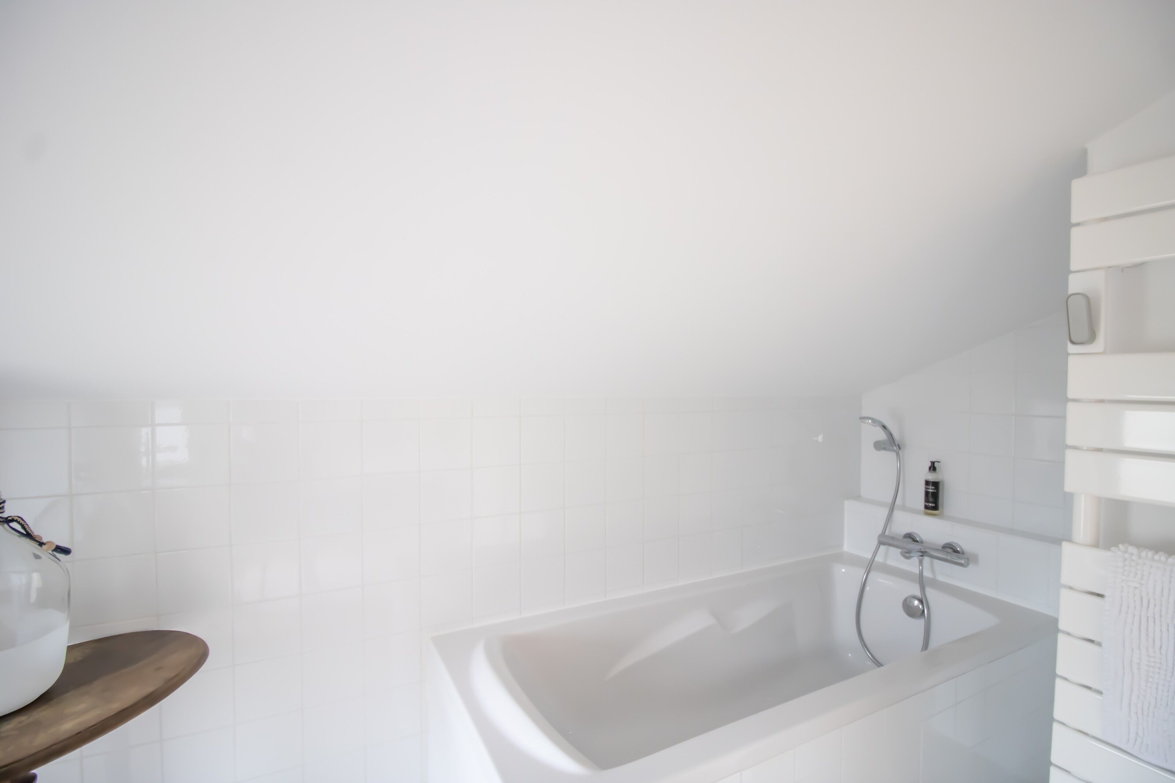 Une salle de bain moderne avec une baignoire, un banc en bois et un mur recouvert de carreaux blancs.