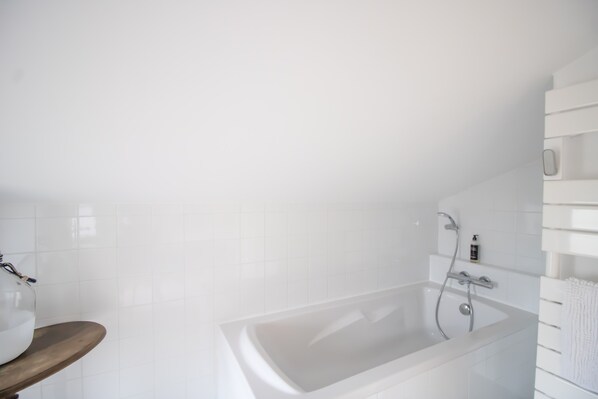 Ein modernes Badezimmer mit einer Badewanne, einer Holzbank und einer weißen Fliesenwand.