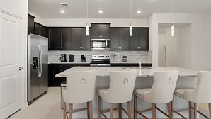 A modern kitchen with dark cabinets, stainless steel appliances, and a marble island with bar stools. - Luxurious 5BD Space at Windsor Cay Resort (Clermont)