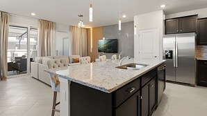 A modern kitchen with a large island, stainless steel appliances, and a flat-screen TV. - Luxurious 5BD Space at Windsor Cay Resort (Clermont)
