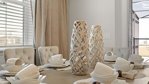 A dining table set for a meal with white plates, bowls, and cutlery. There are two tall, woven candle holders on the table. - Luxurious 5BD Space at Windsor Cay Resort (Clermont)