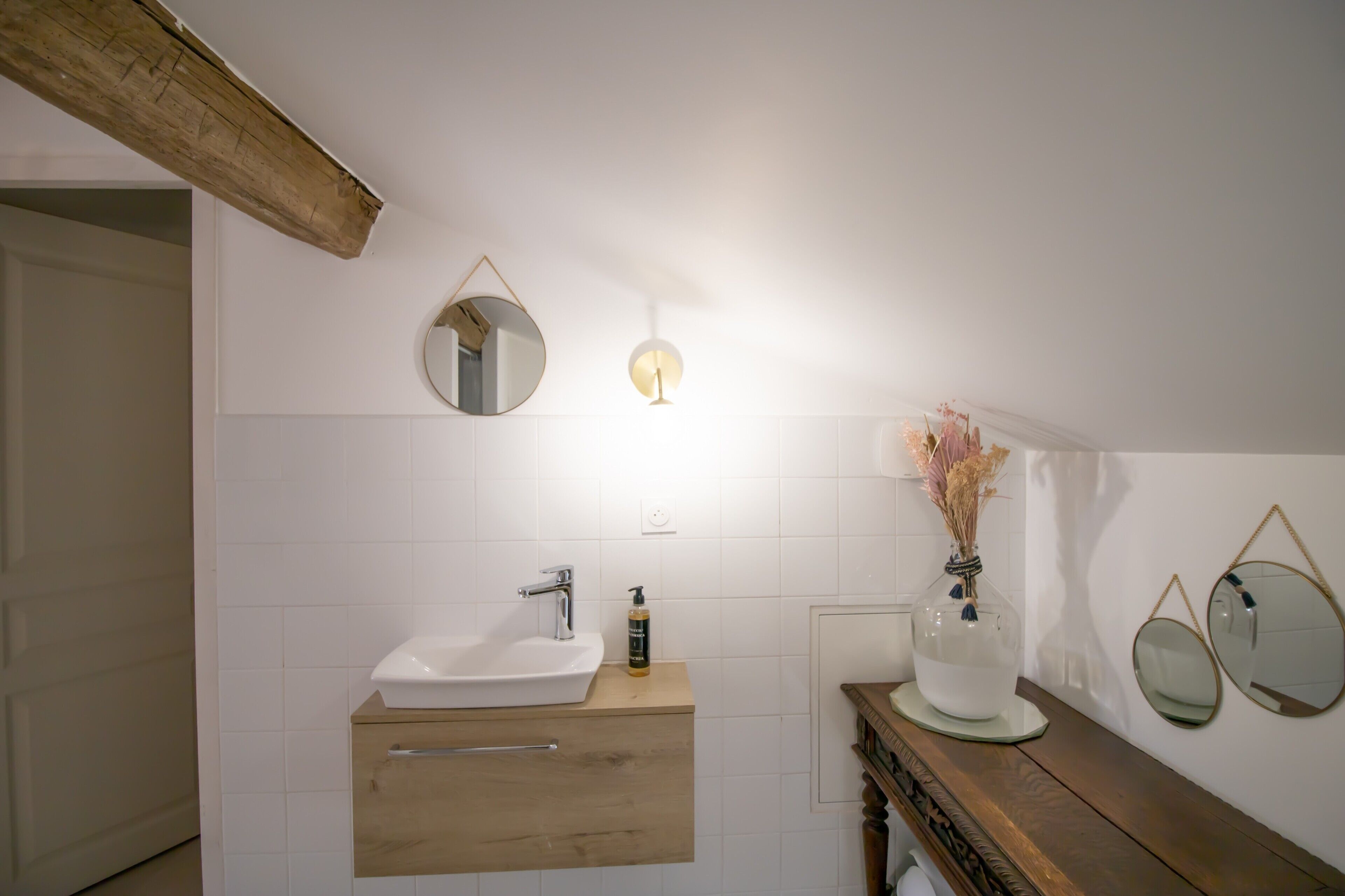 A bathroom with a wooden vanity, a white sink, a mirror, and a wall-mounted light fixture.
