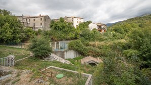 Un village perché sur une colline, avec des bâtiments traditionnels en pierre, un petit pont et une végétation luxuriante.