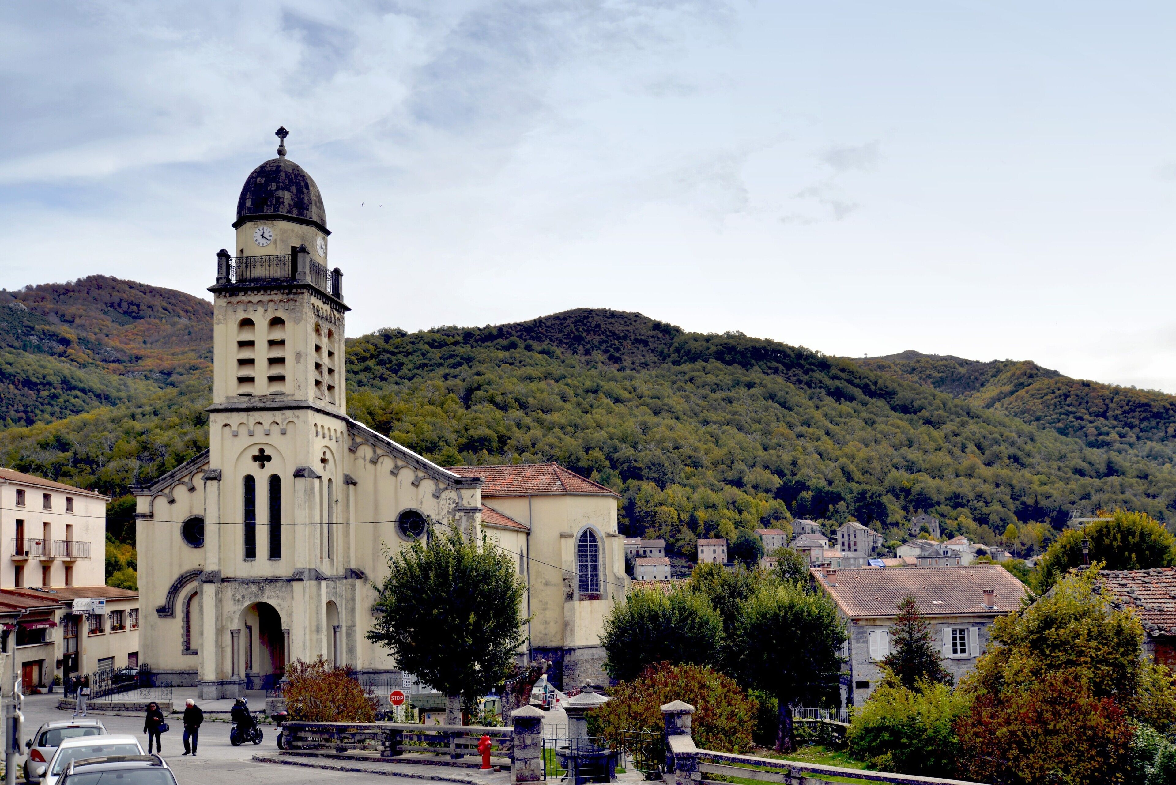 Une église dotée d’un clocher, entourée d’arbres et de bâtiments.