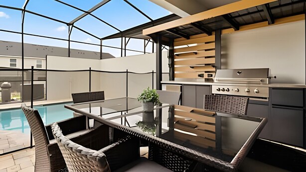 An outdoor kitchen with a grill, dining table, and chairs, overlooking a swimming pool. - Modern 6-BR Home w/ Summer Kitchen - Solara Resort (Kissimmee)