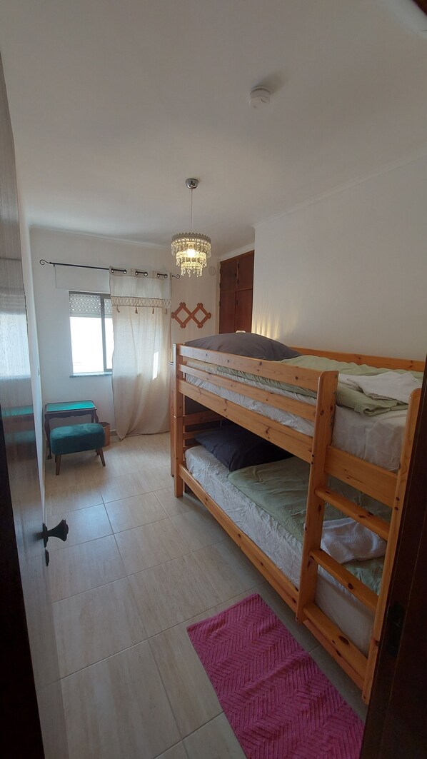 A bunk bed room with a wooden floor, a pink rug, a small table, and a hanging light fixture.