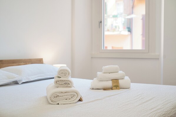 A neatly made bed with rolled white towels and a small stack of towels with a label.
