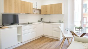 A modern kitchen with white cabinetry, a built-in TV, and a glass dining table. - Mascari Suites - Saxum (Lecco)