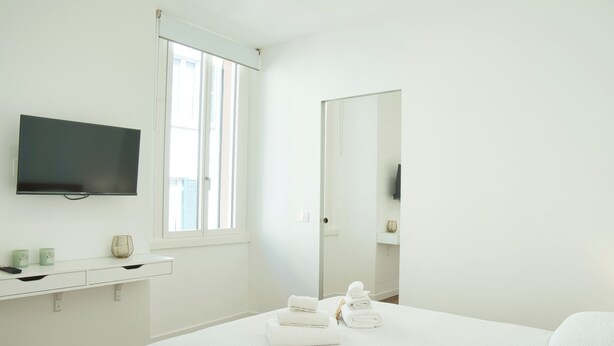A bedroom with a bed, a TV mounted on the wall, a window, and a mirror. - Mascari Suites - Saxum (Lecco)