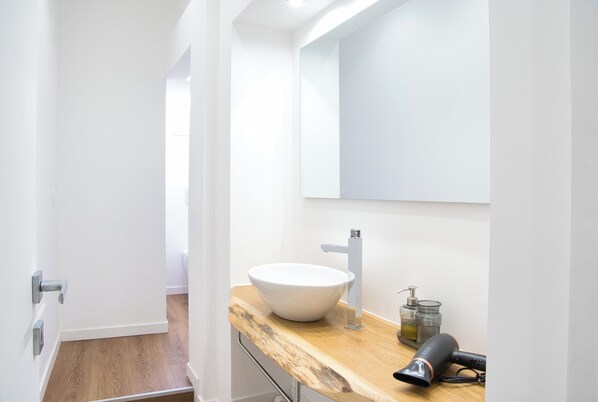 A modern bathroom with a white sink, wooden countertop, and a mirror.