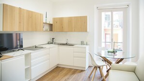 A modern kitchen with white cabinets, a built-in oven, and a glass dining table. - Mascari Suites - Saxum (Lecco)
